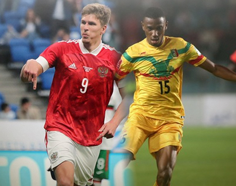 На изображении два футболиста в форме разных команд: игрок в красной форме с номером 9 и игрок в желтой форме с номером 15. Они находятся на поле в момент игры