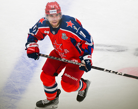 Хоккеист в красной форме с синими и белыми деталями на льду. Он держит клюшку и двигается в игре. На форме номер 17 и логотип команды